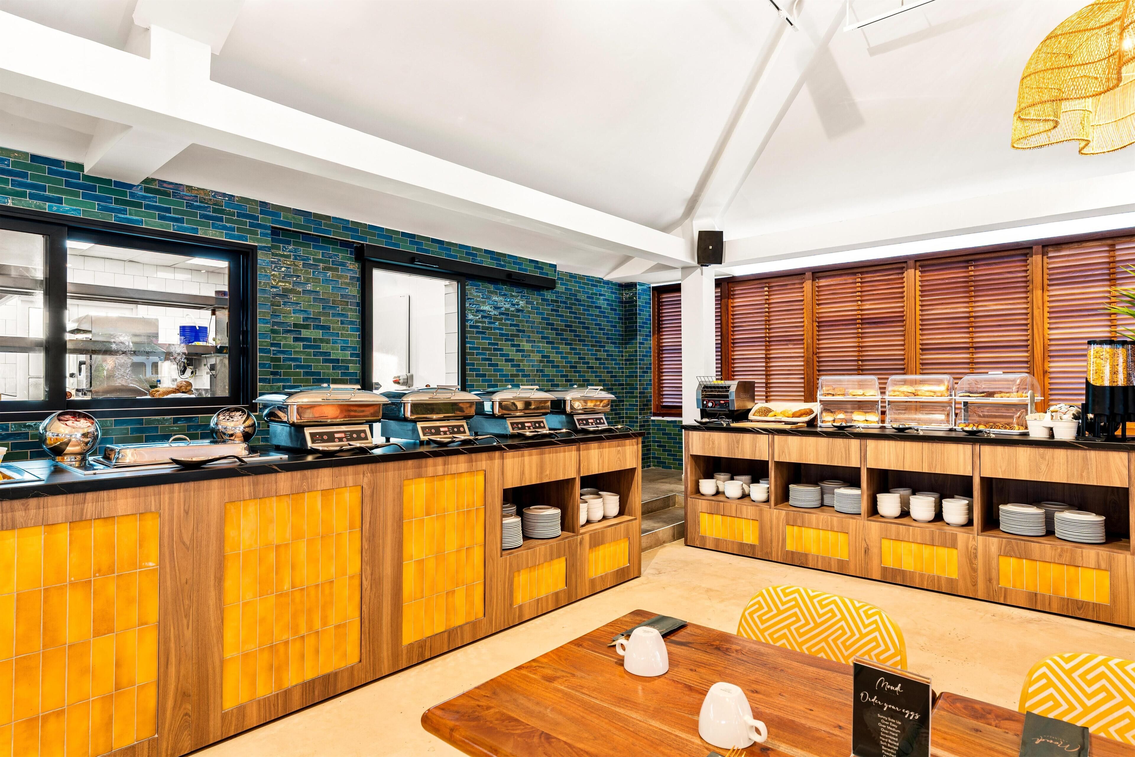 Un bar de cuisine avec un revêtement mural bleu en carreaux, des armoires en bois et une variété d’aliments pour le petit-déjeuner.