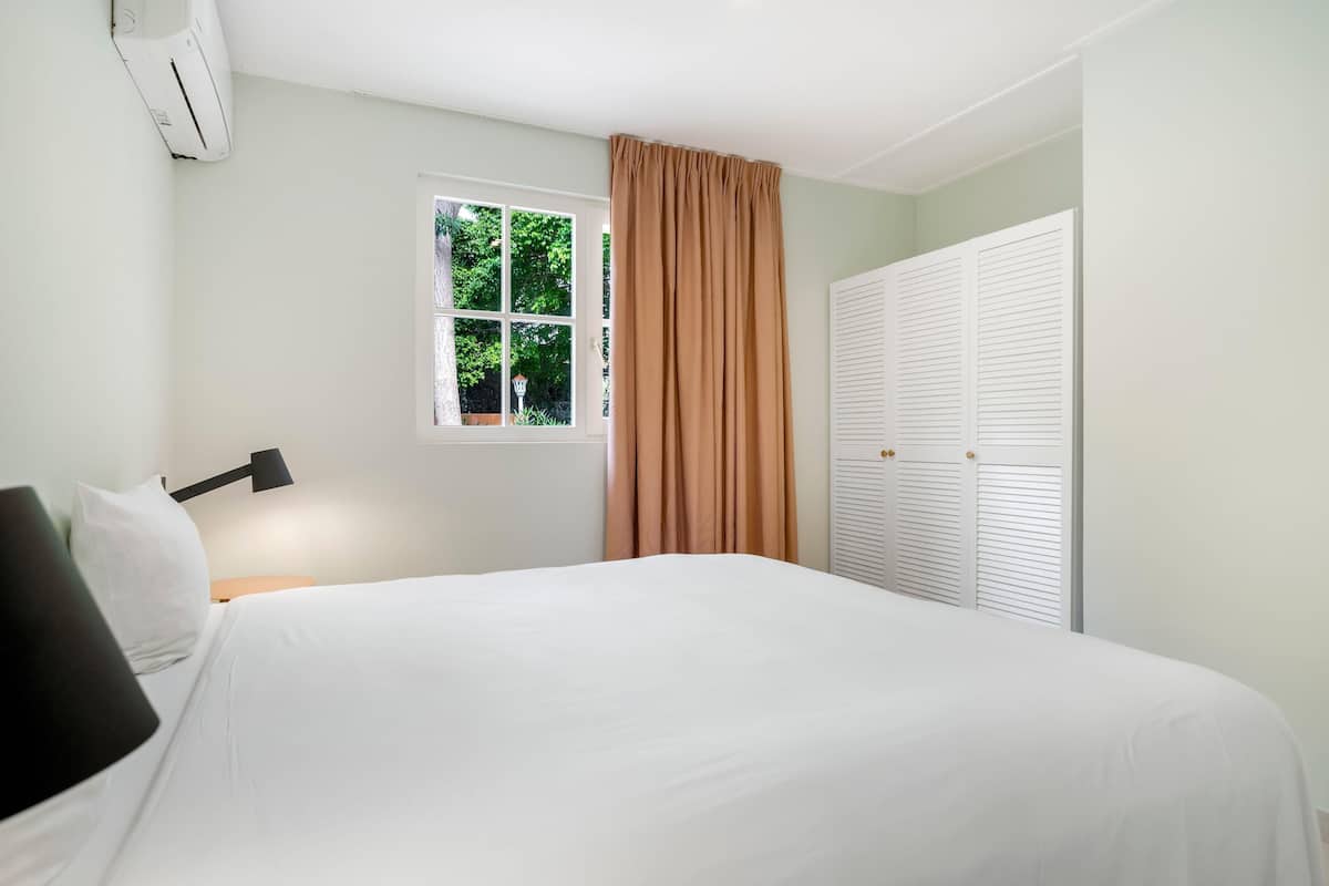 A bedroom with a bed, a window with curtains, a bedside lamp, and a closet.