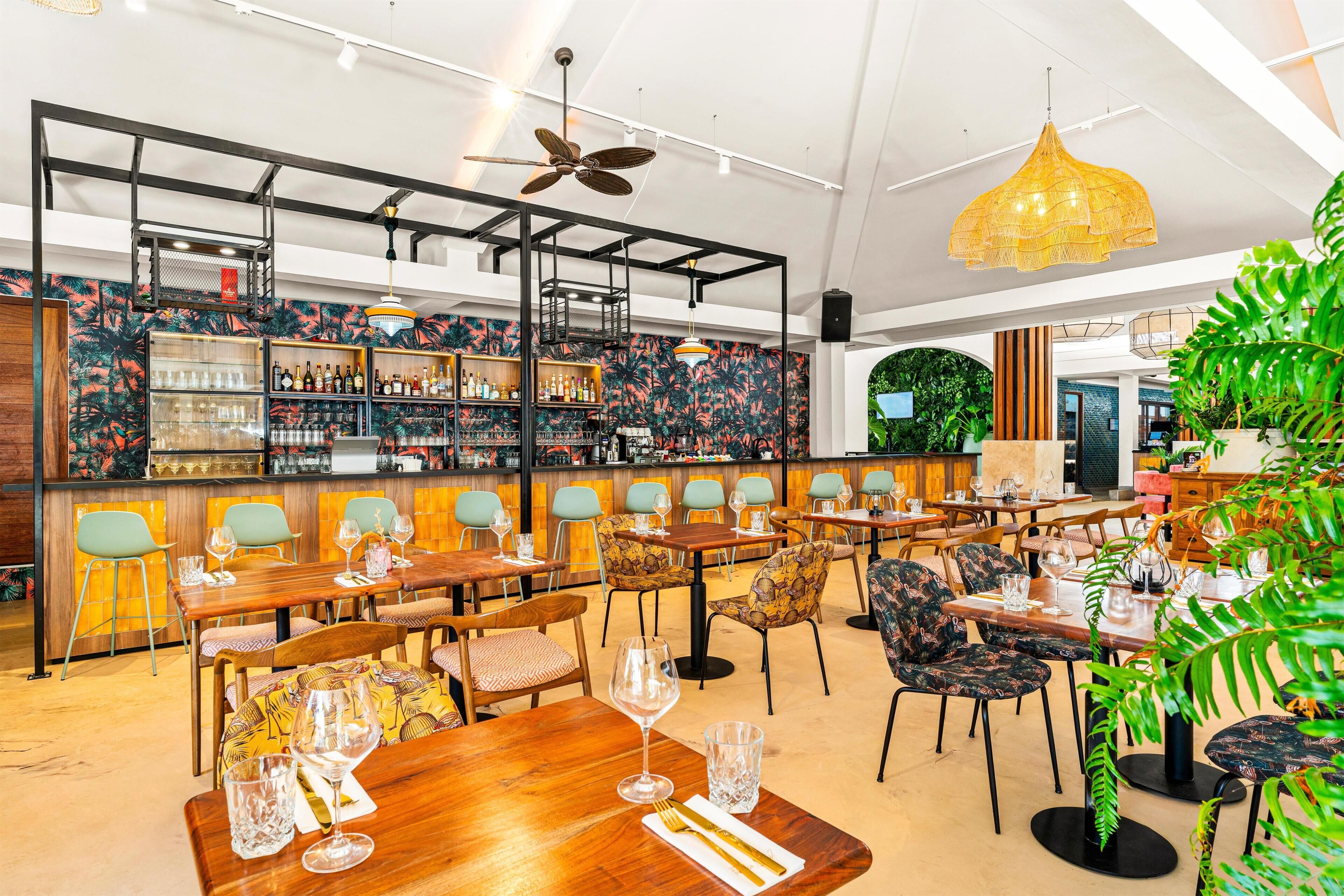 Un restaurante con mesas y sillas de madera, una zona de bar y un ventilador de techo.
