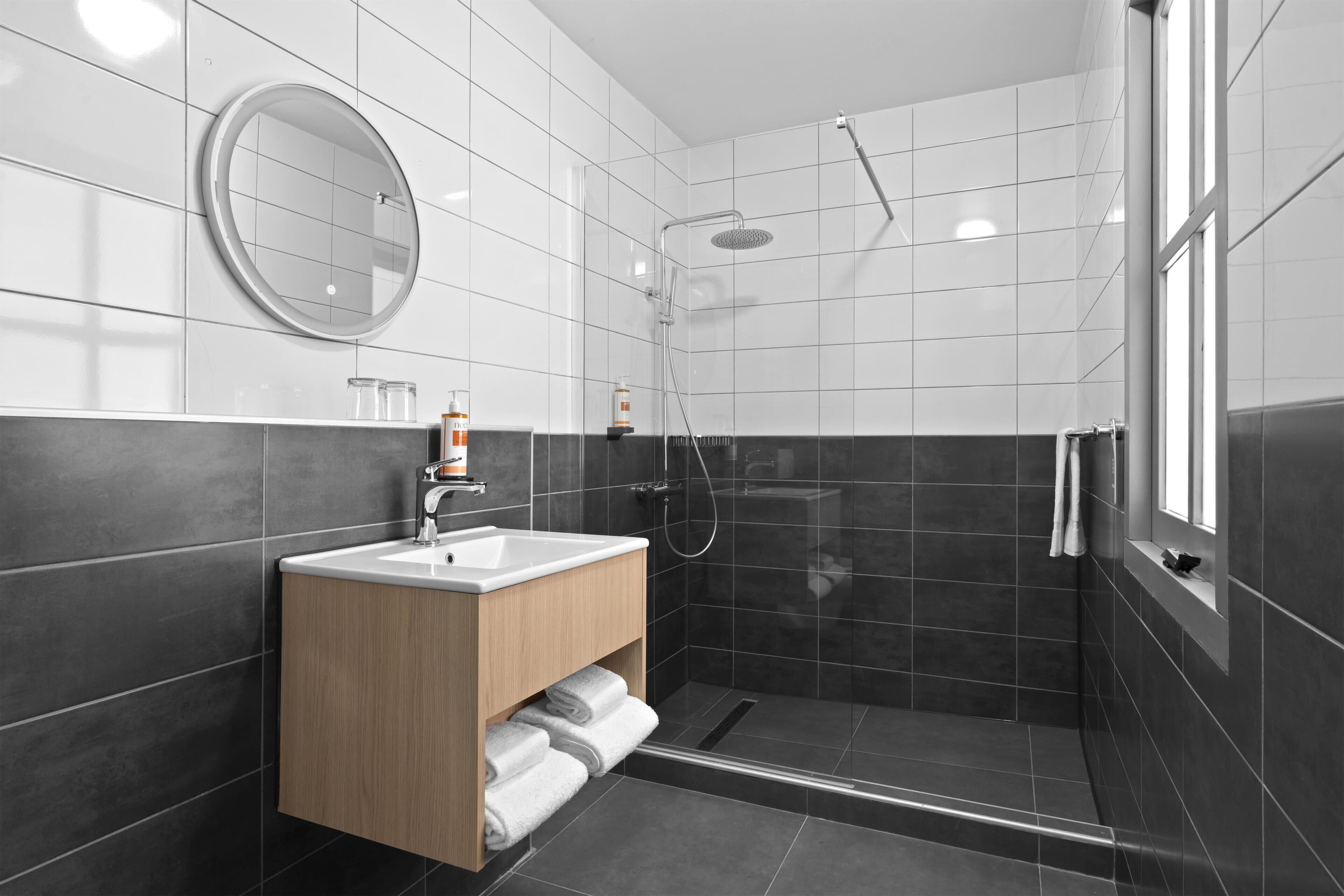 Un baño moderno con ducha, lavabo, espejo y ventana.