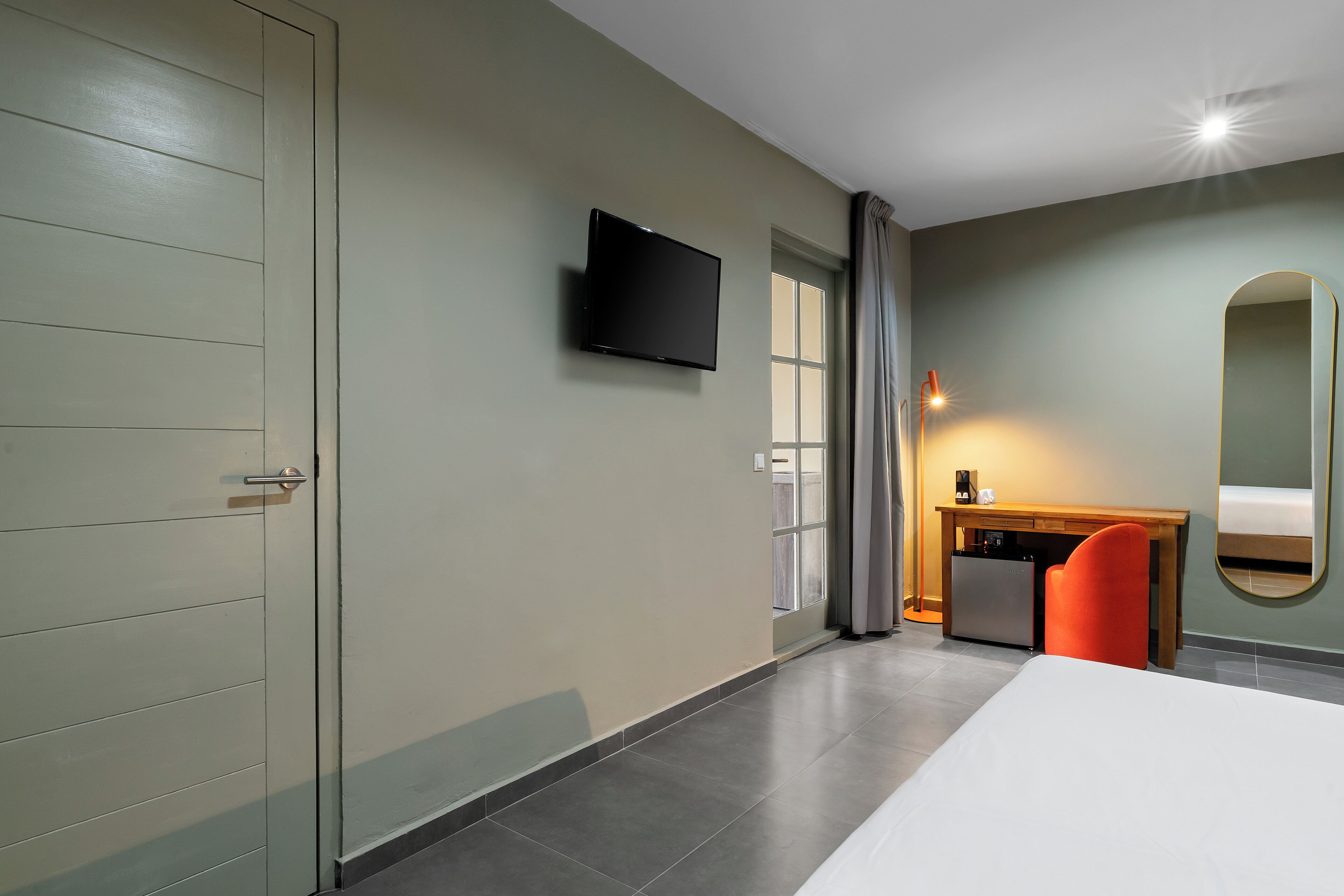 Quarto de hotel com cama, escrivaninha, cadeira, televisão e espelho.