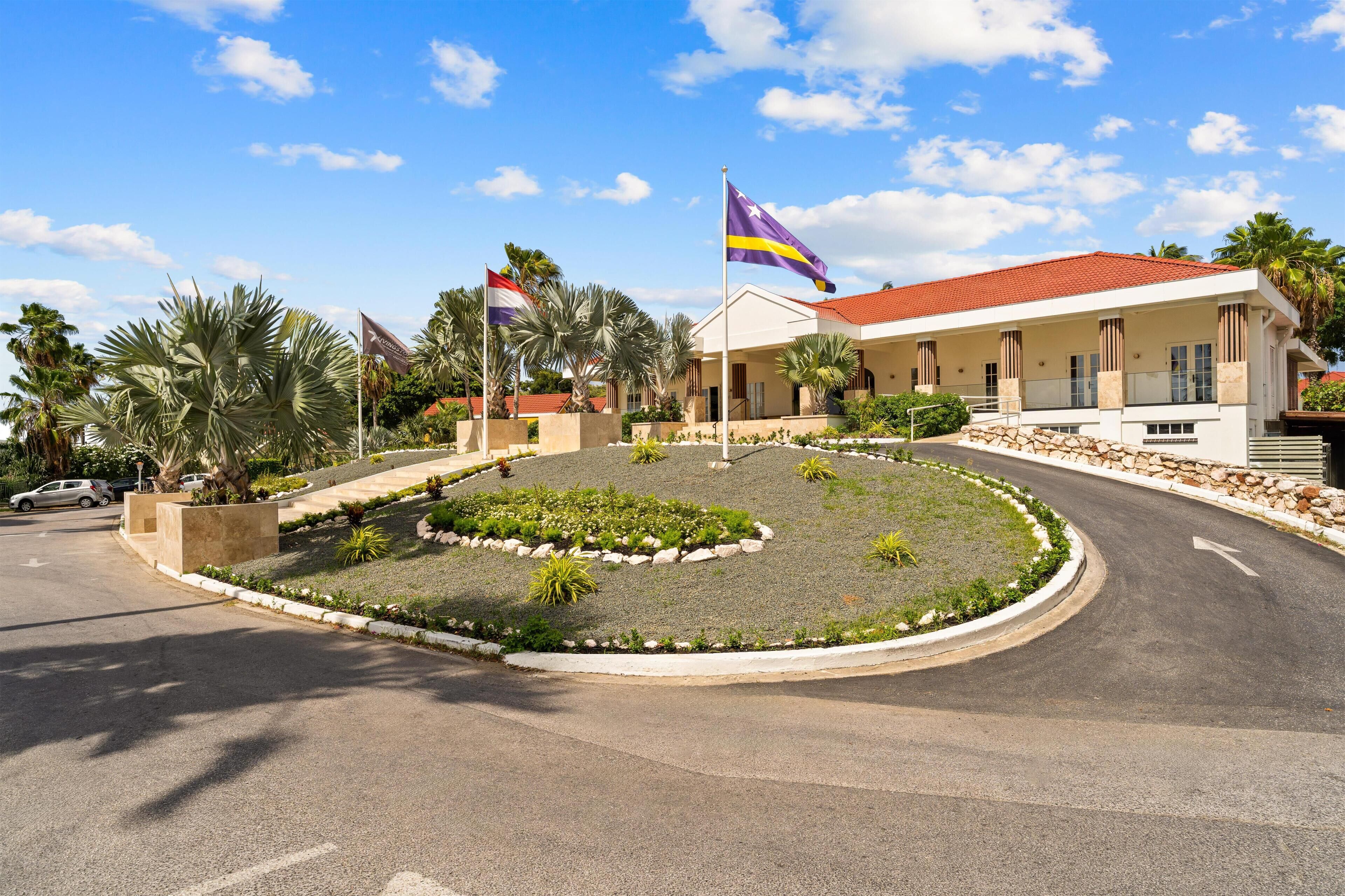 A hotel entrance with a landscaped garden, palm trees, and flags.