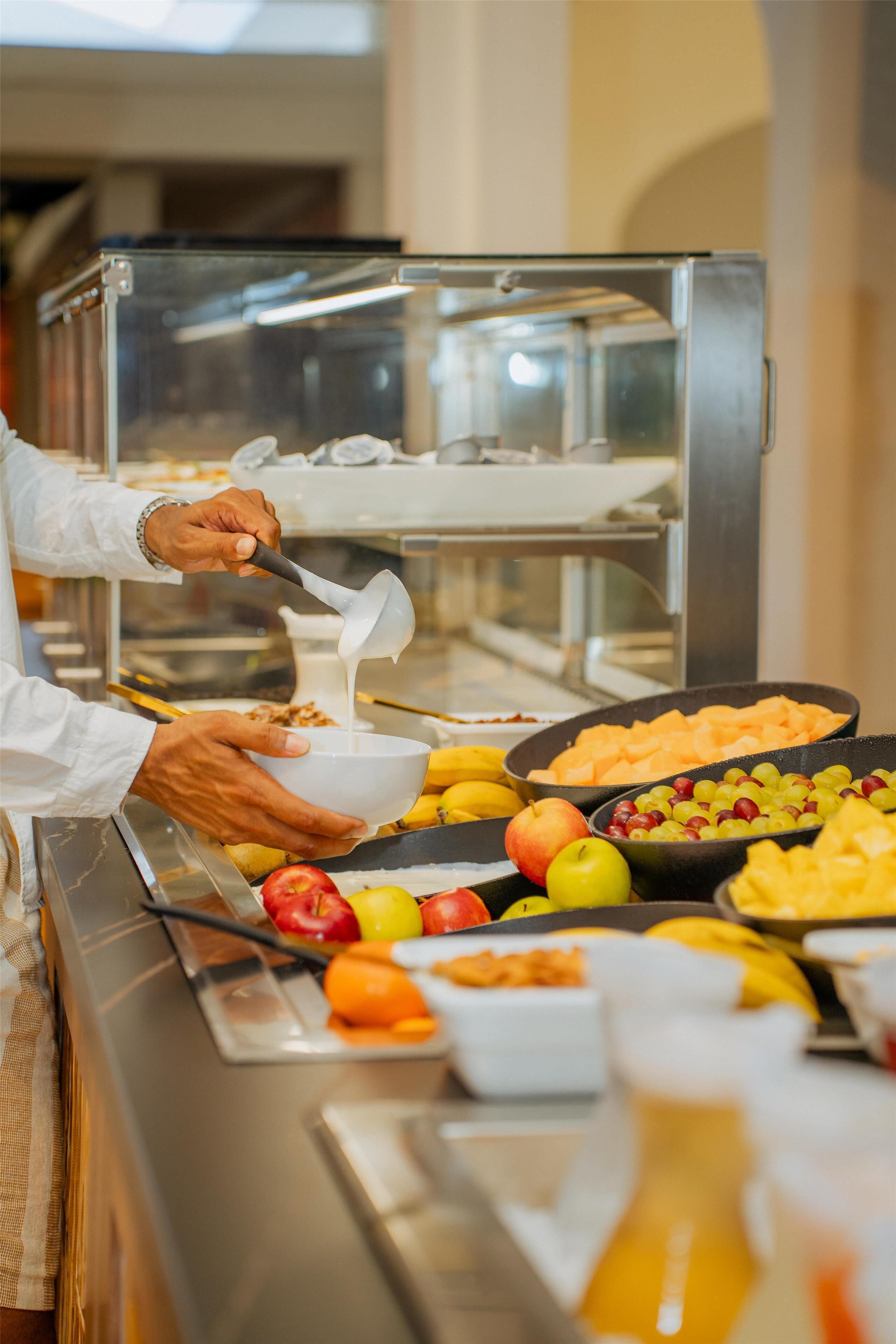 Una mesa de buffet con diferentes frutas y una persona sirviendo comida.
