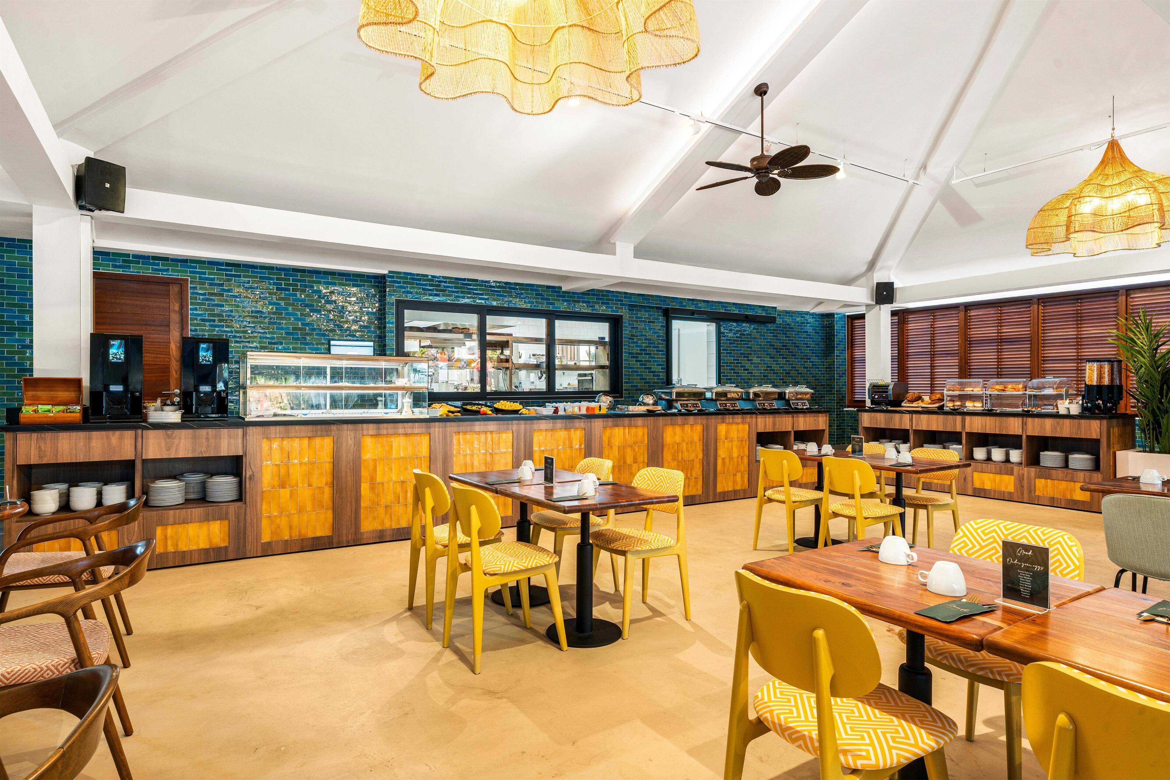 Un restaurante con mesas de madera y sillas amarillas, una barra con productos alimenticios y una pared de azulejos azules.