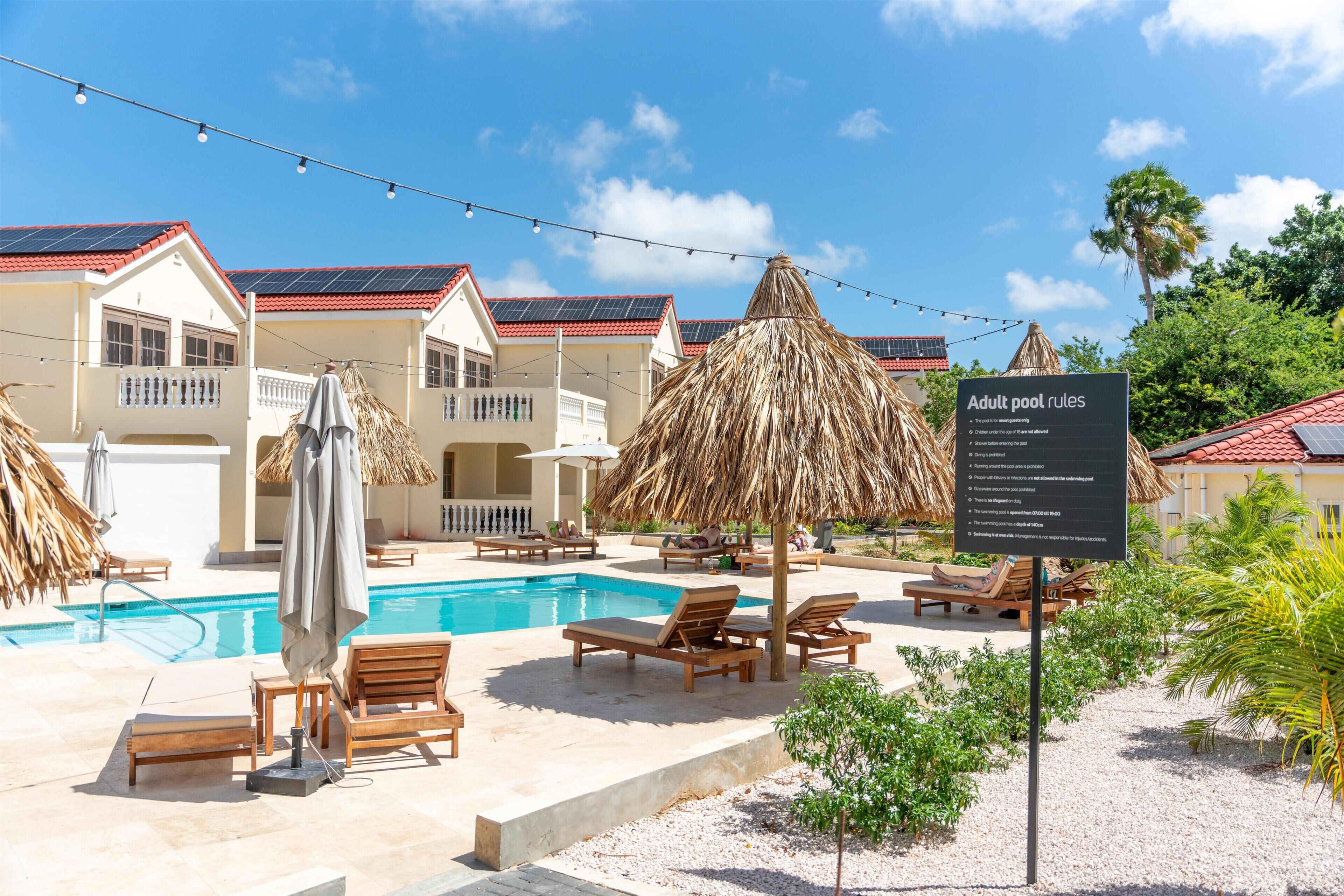 A pool area with lounge chairs, umbrellas, and a sign listing adult pool rules.
