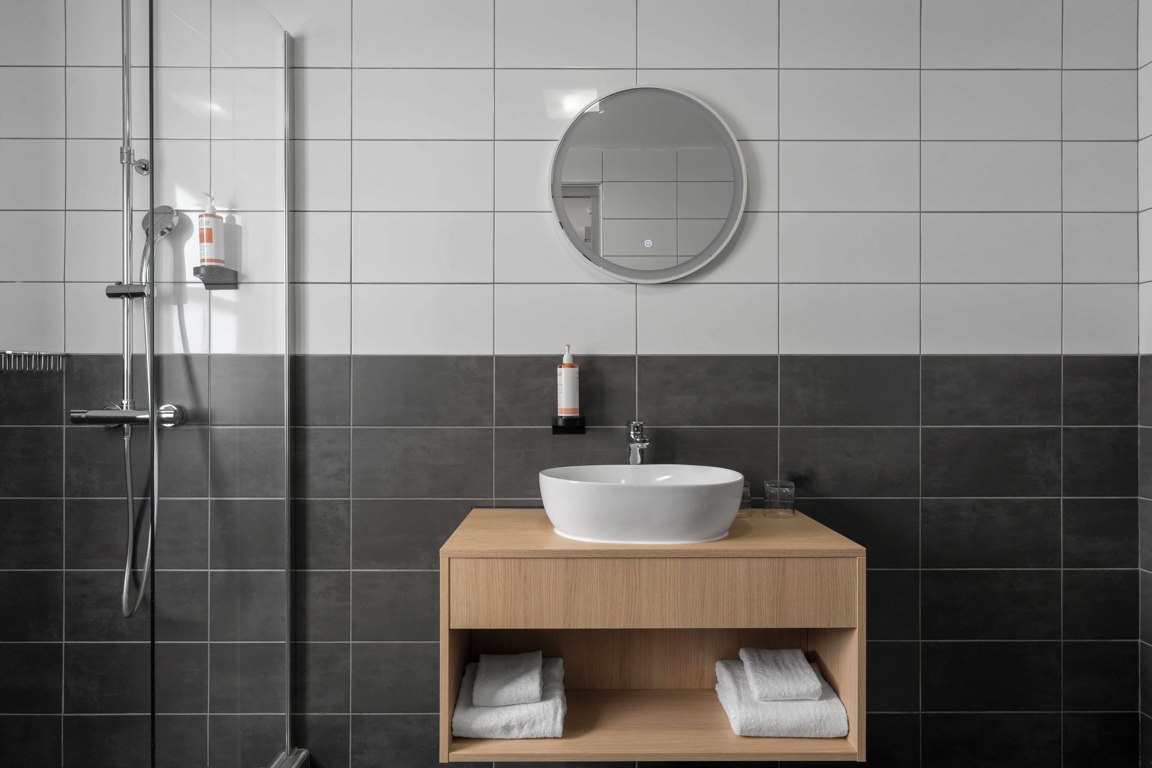 Ein modernes Badezimmer mit rundem Spiegel, einem Aufputzbecken und einer Duschkabine.