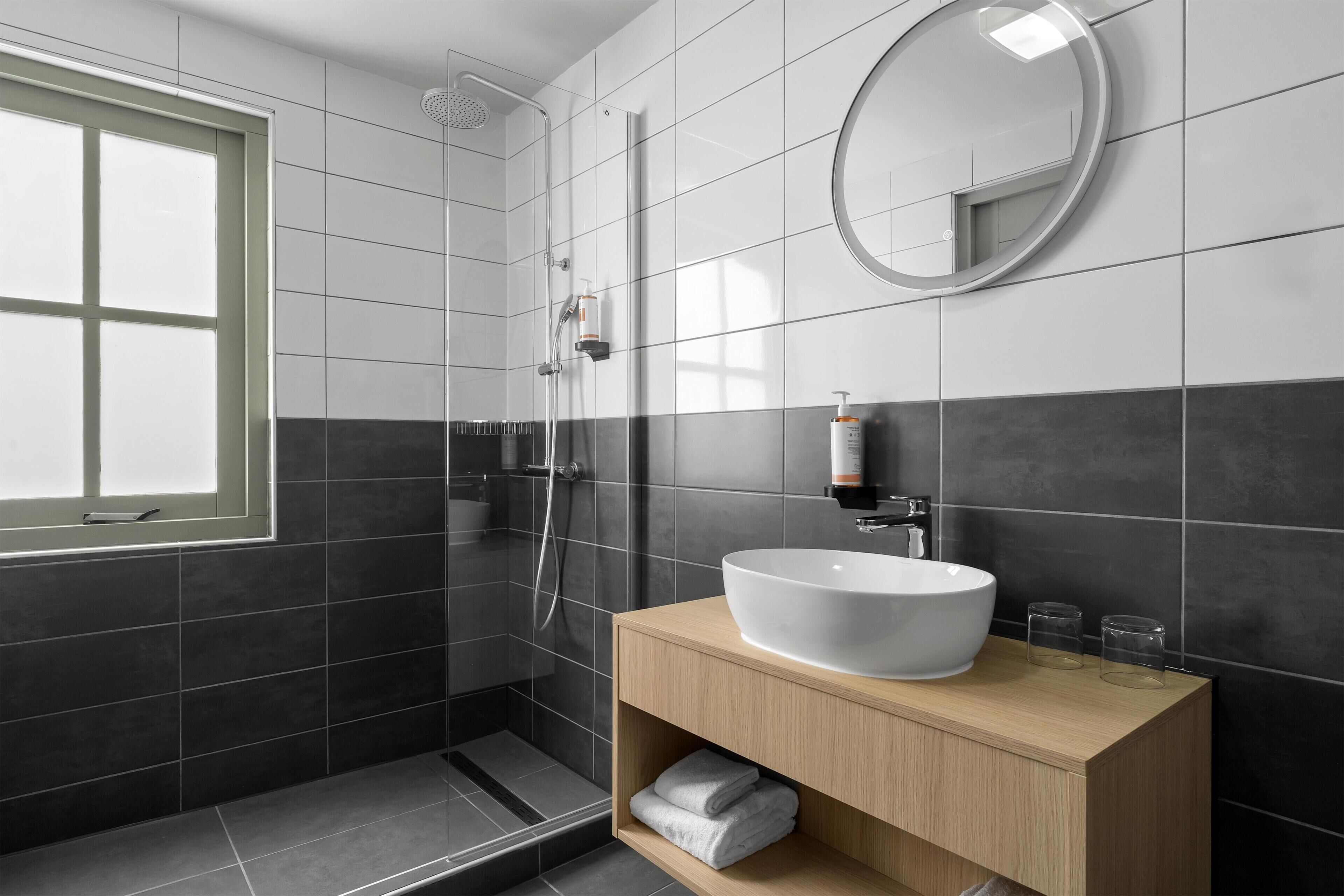 A modern bathroom with a large white sink, a mirror, and a shower area.