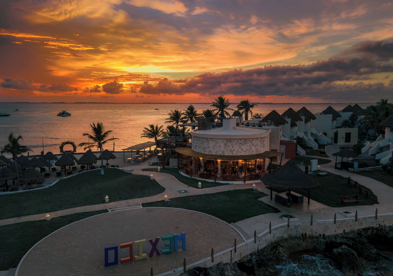 Un complexe hôtelier avec vue sur la plage, une piscine et un bâtiment sur lequel on peut clairement lire le mot « MEXICO ».