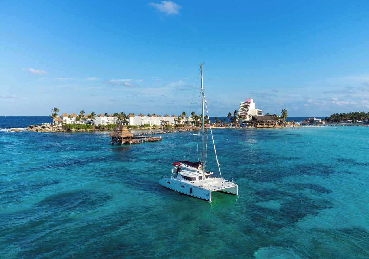 A white sailboat on turquoise waters with a coastal town in the background.