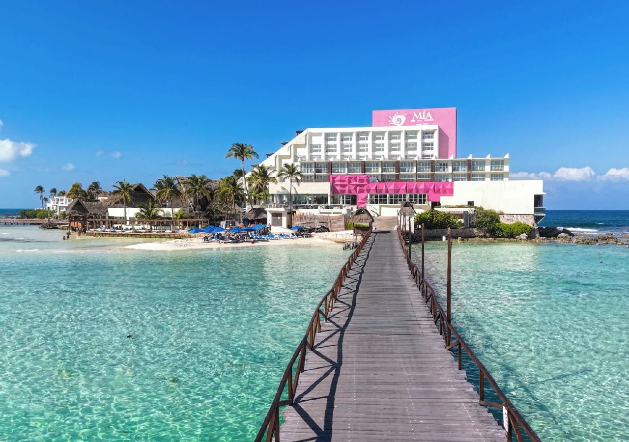 A wooden pier leading to a hotel with a beach view.