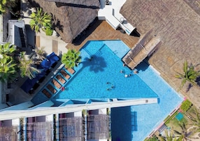 Vista aérea de un hotel con una gran piscina, varias áreas de descanso y palmeras.