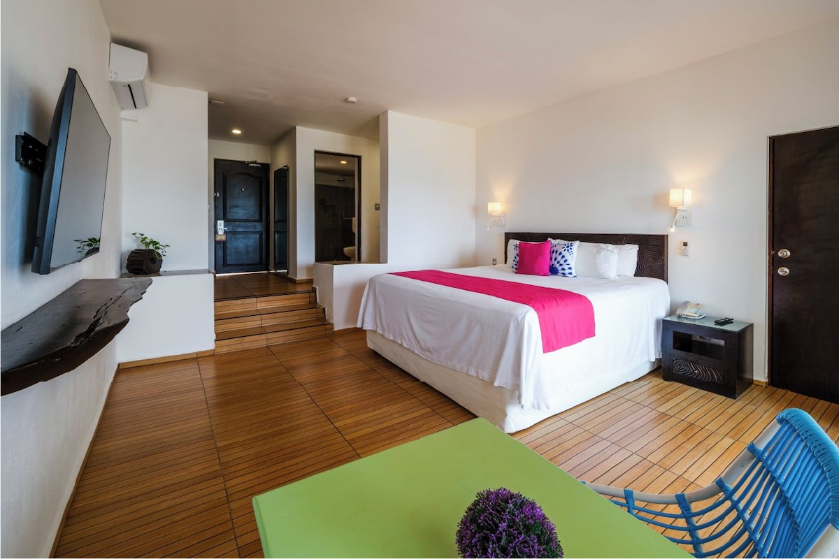 Una habitació d'hotel amb llit, taulella de nit, cadira i televisió penjada a la paret.