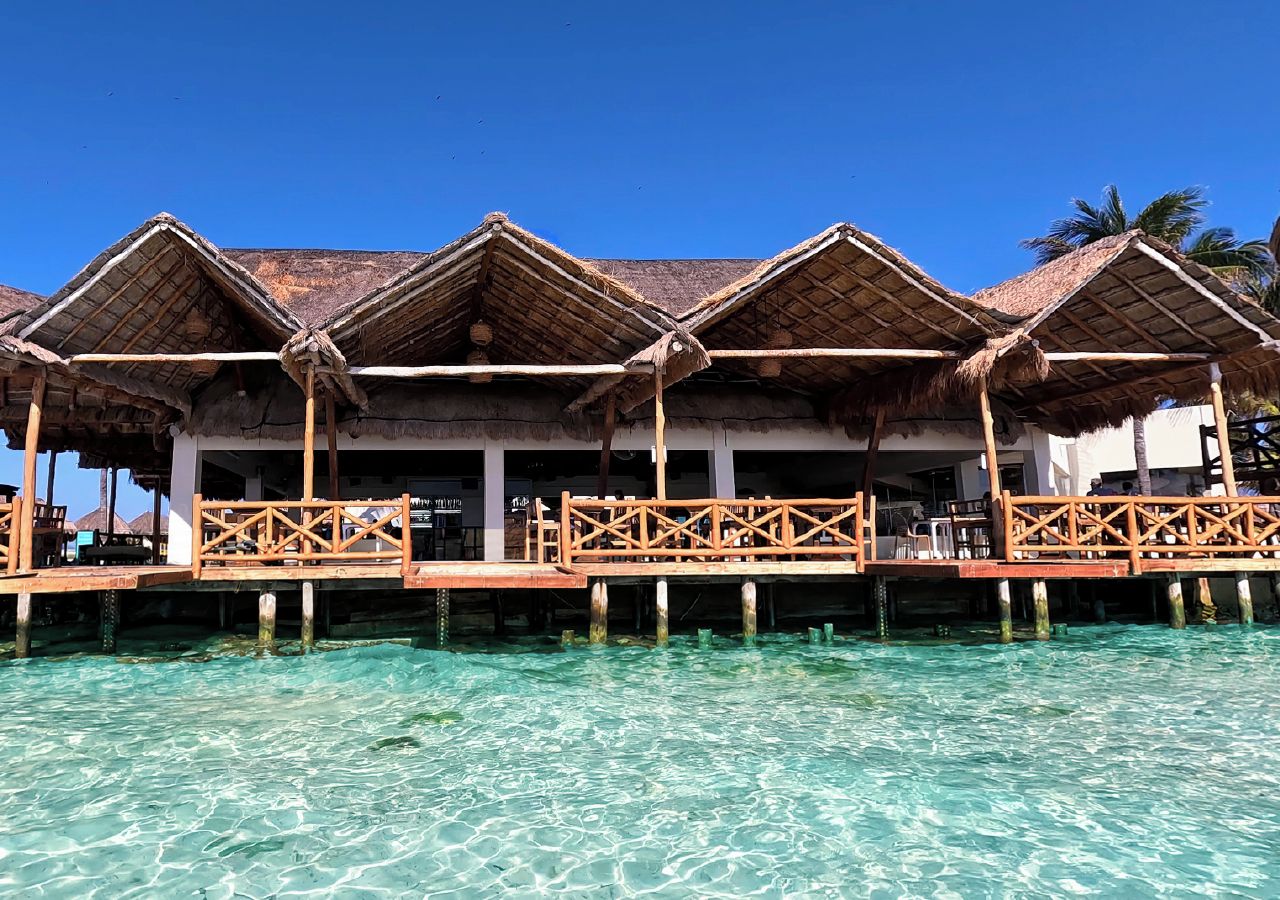 Overwater bungalows with thatched roofs and wooden railings, connected by a wooden walkway over clear turquoise water.