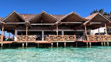 Overwater bungalows with thatched roofs and wooden railings, connected by a wooden walkway over clear turquoise water.