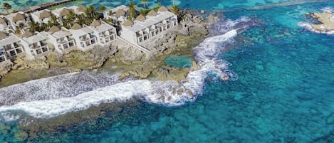 Vista aérea de un complejo turístico costero con bungalows sobre el agua, aguas turquesas cristalinas y un muelle que se adentra en el mar.