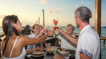 Un grupo de personas brindando con bebidas en una mesa de madera junto al agua.