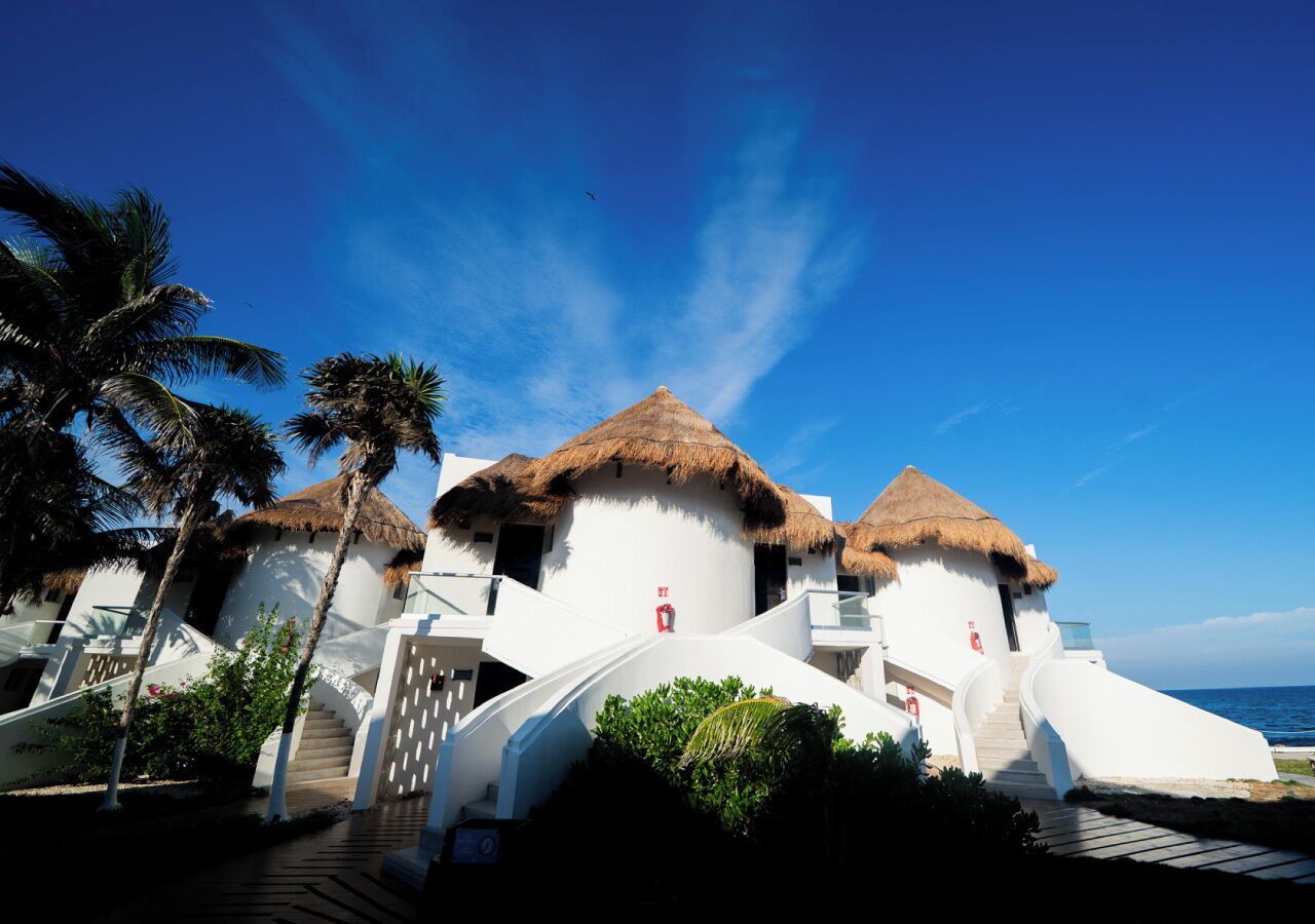 Un resort con edificios de techo de paja, una escalera que conduce a la entrada y vista al mar.