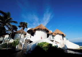 Un resort con edificios de techo de paja, una escalera que conduce a la entrada y vista al mar.