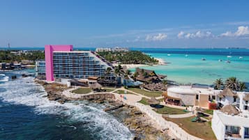Un hotel costero con un edificio rosa destacado, servicios en la playa y aguas turquesas cristalinas.
