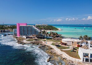 Ein Küstenhotel mit einem markanten rosafarbenen Gebäude, Annehmlichkeiten direkt am Strand und klarem türkisblauem Wasser.