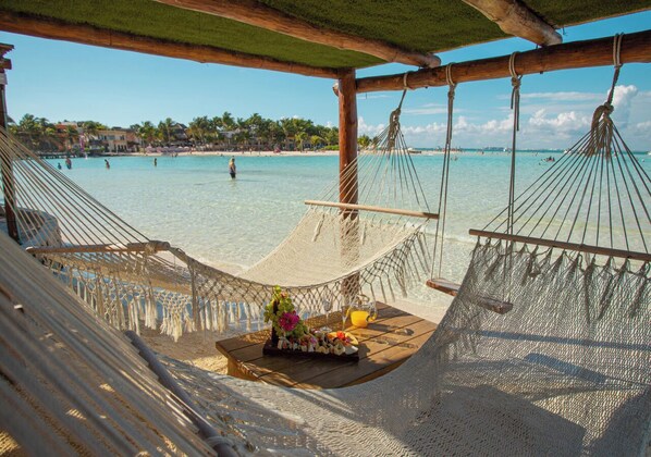 A beach with hammocks and a table with flowers and a drink. - Mia Reef Isla Mujeres - All Inclusive (Isla Mujeres)
