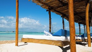 A beach with a wooden structure, a white lounge chair, and a clear view of the ocean.