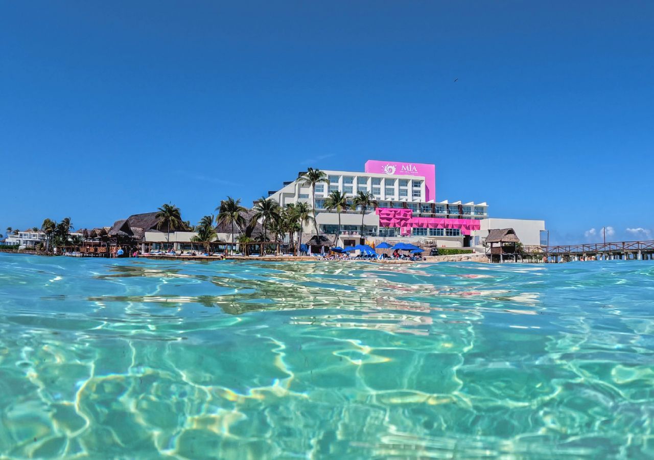 Un resort con vistas despejadas al océano, un edificio rosa destacado y varias palmeras.