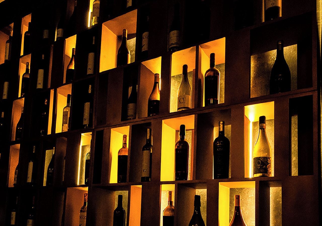 Un mur composé d’étagères éclairées, où sont exposées de nombreuses bouteilles de vin.