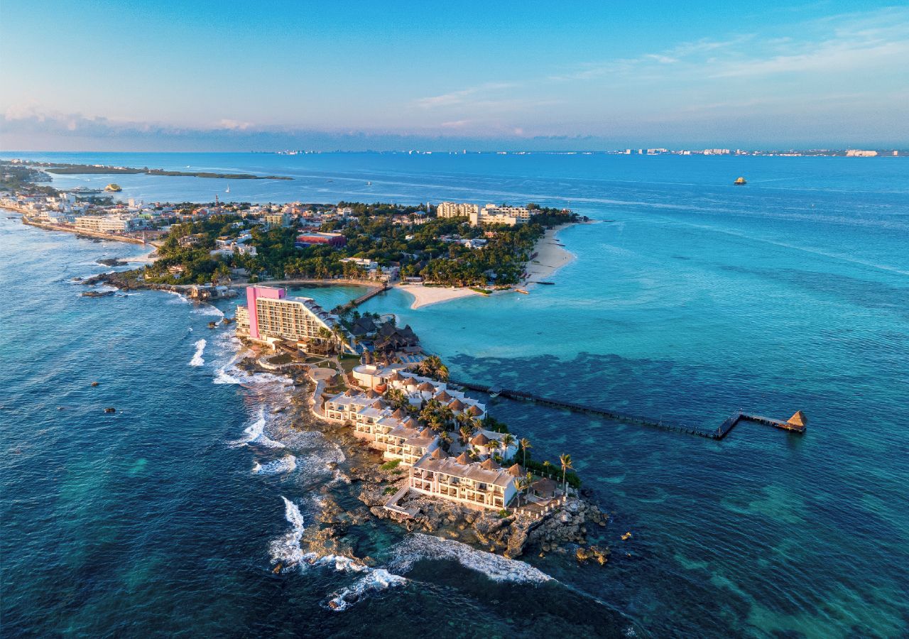 Un complejo turístico frente al mar con villas privadas en la playa, un muelle y una pequeña isla con edificios.