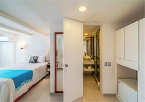 A hotel room with a bed, a bedside table, a wardrobe, and a bathroom with a sink and mirror.