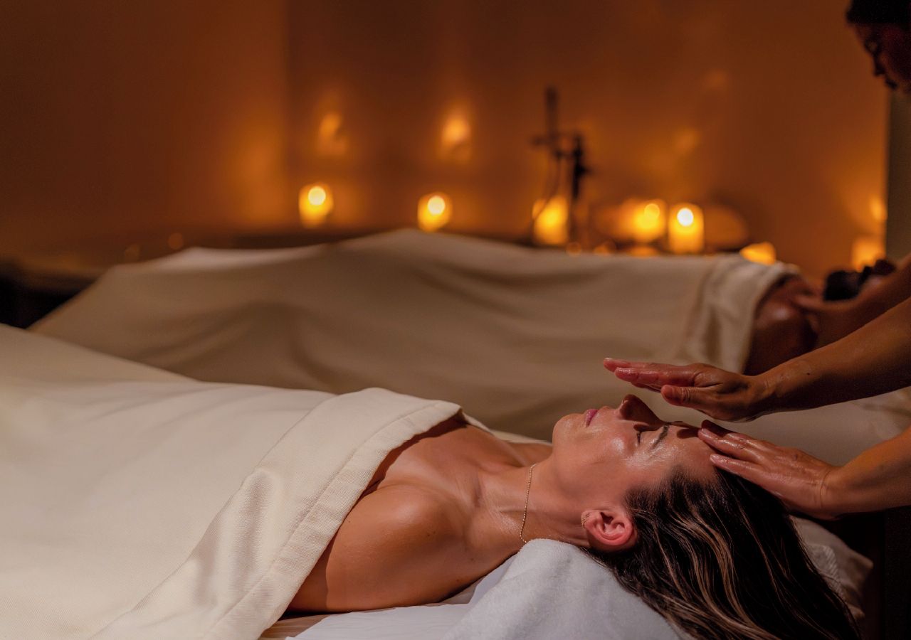 Iemand ontvangt een massage in een ruimte met een bed en kaarsen op de achtergrond.