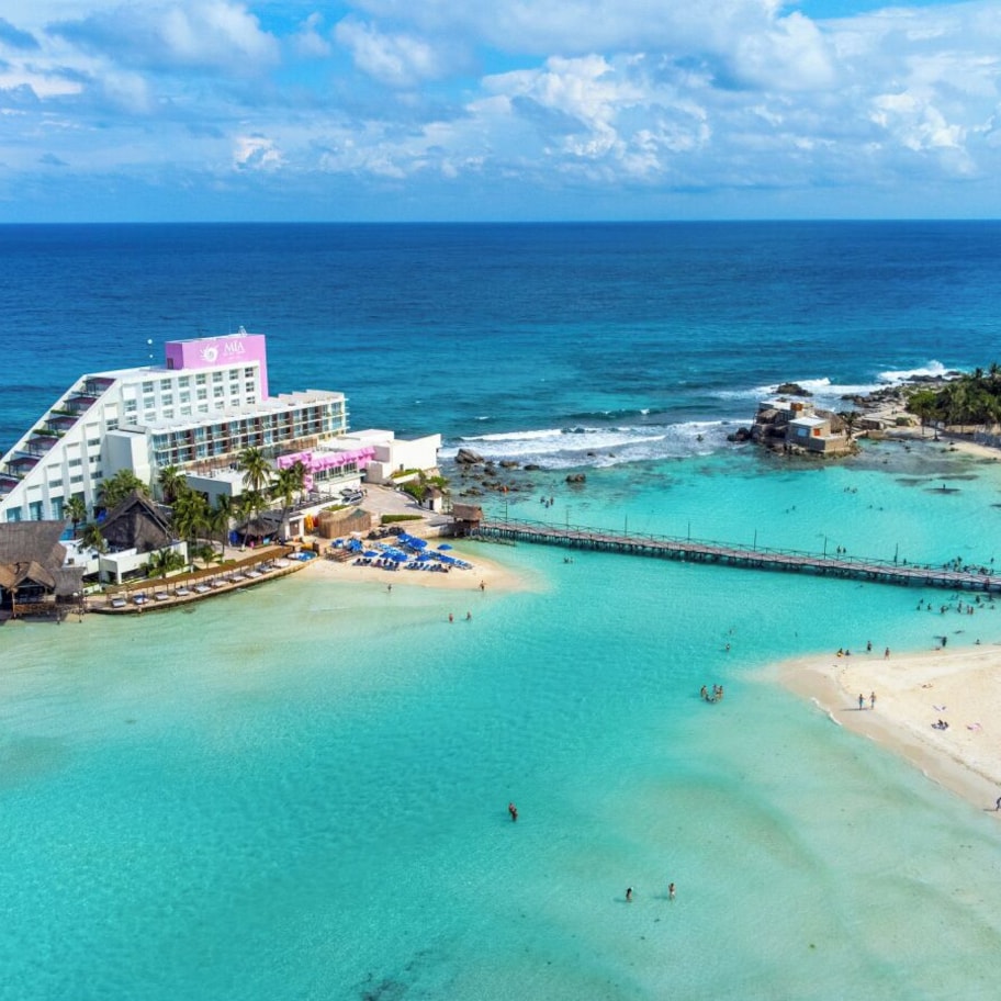 A resort with a beach, a pier, and a hotel with a view of the ocean.