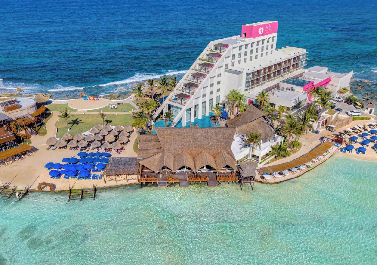 A resort with a pool, beach area, and a building with a prominent pink sign.