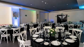 Un salón de banquetes con mesas redondas dispuestas para cenar, sillas blancas y mantel negro.