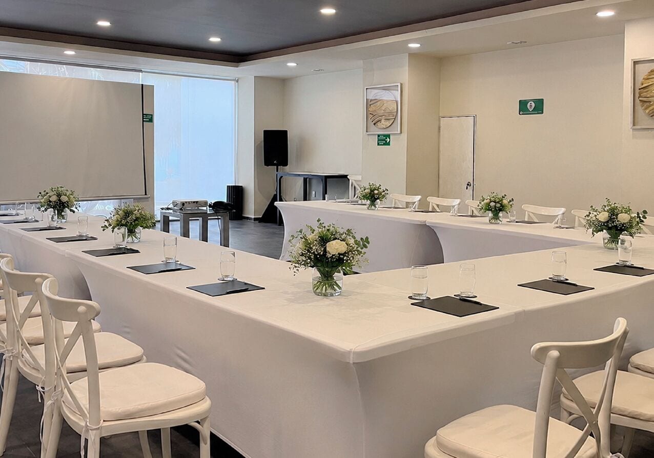 A conference room with a long table, white chairs, and floral centerpieces.