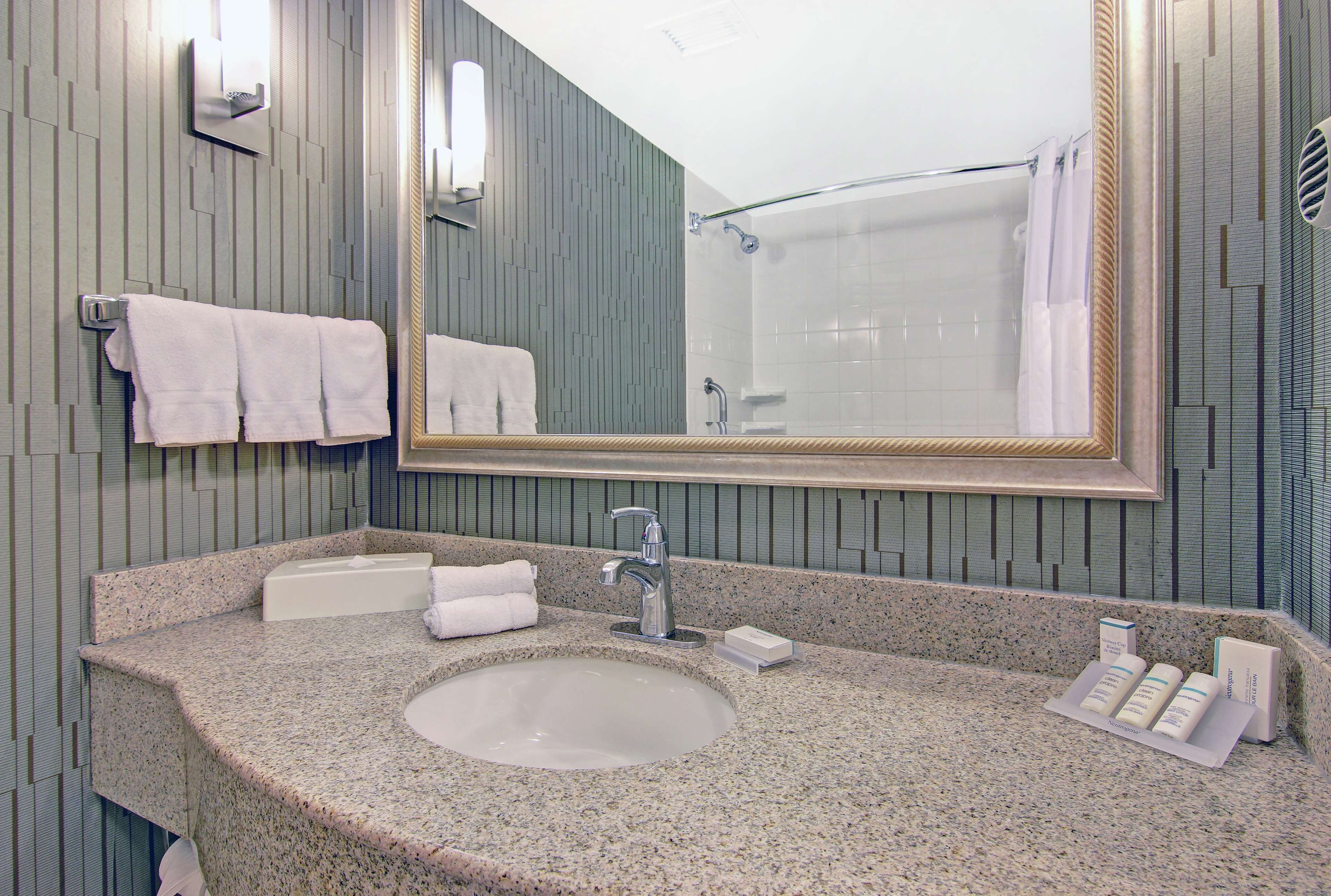 A bathroom with a granite countertop, a sink, a mirror, and a shower.