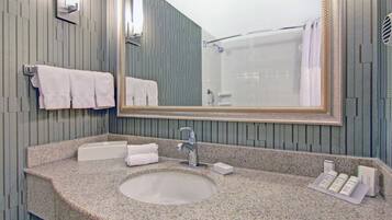 A bathroom with a granite countertop, a sink, a mirror, and a shower.