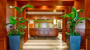 A hotel lobby with a reception desk, large potted plants, and a tiled floor. - Hilton Garden Inn Toronto/Markham (Markham)