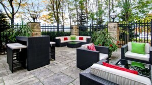 An outdoor patio with wicker furniture, stone pillars, and a black metal fence. - Hilton Garden Inn Toronto/Markham (Markham)