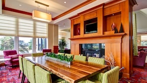 A spacious dining area with a wooden table and green upholstered chairs, a fireplace, and large windows offering a view of the outdoors.