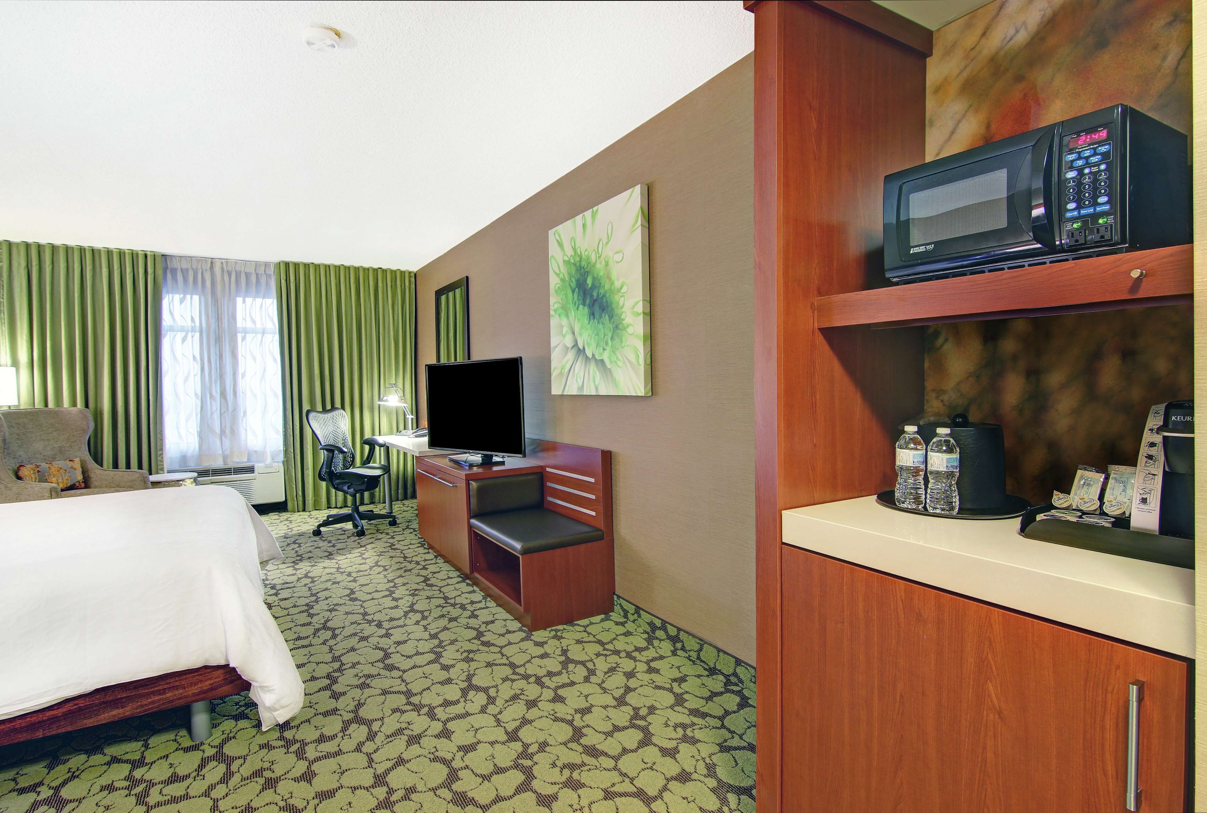 A hotel room with a bed, a desk with a computer, a television, a microwave, and a coffee machine.