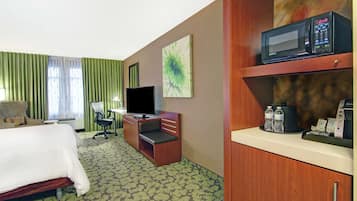 A hotel room with a bed, a desk with a computer, a television, a microwave, and a coffee machine.
