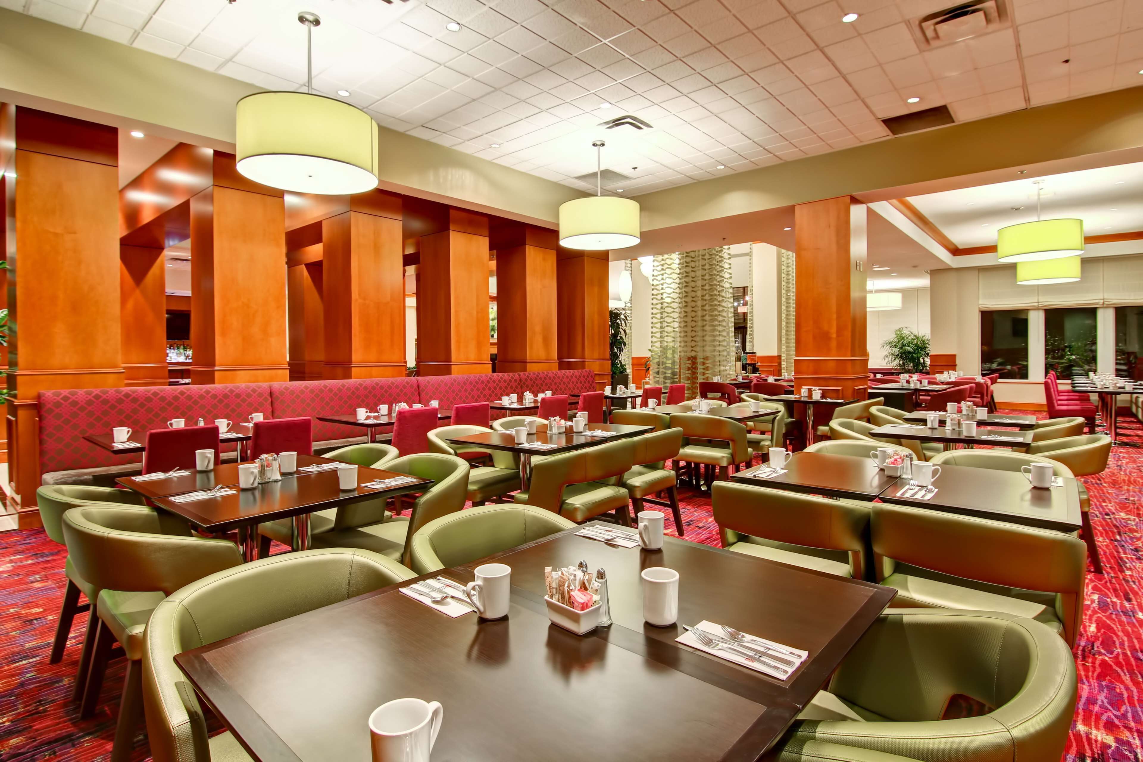 A hotel dining area with multiple tables and booths, red cushioned seating, and green upholstered chairs.