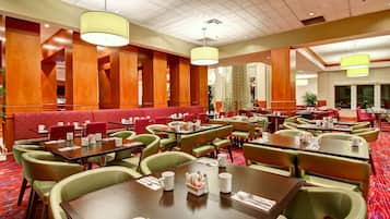 A hotel dining area with multiple tables and booths, red cushioned seating, and green upholstered chairs.