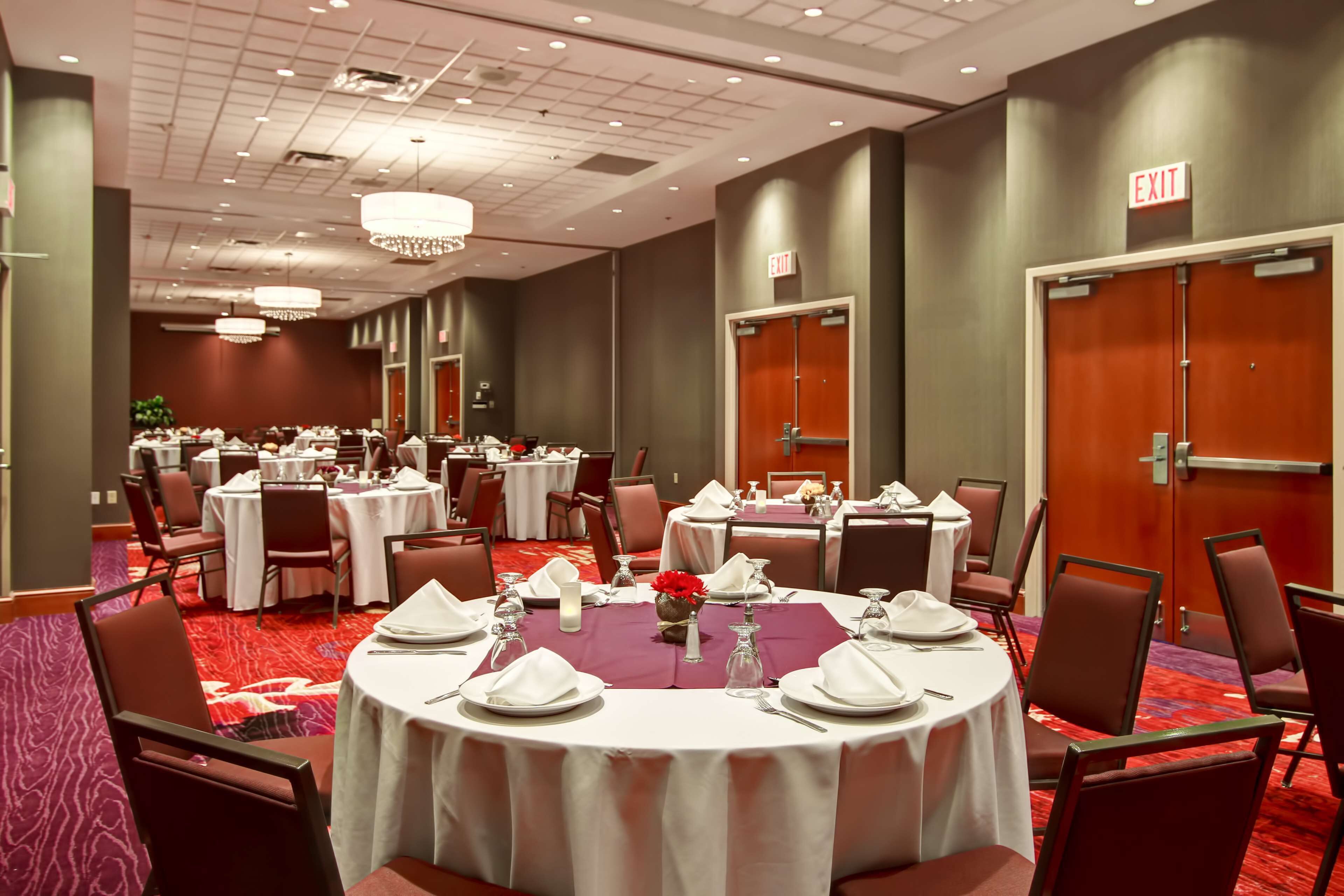 Un salón de conferencias con varias mesas redondas dispuestas para comer, equipado con manteles blancos, servilletas y cubiertos.