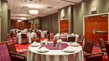 Un salón de conferencias con varias mesas redondas dispuestas para comer, equipado con manteles blancos, servilletas y cubiertos.