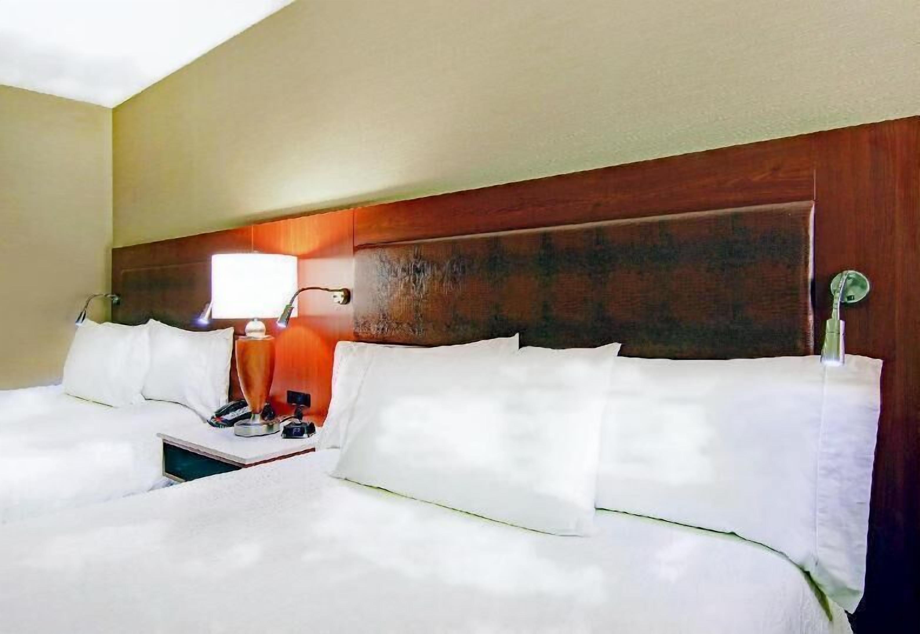 Una habitación de hotel con una cama grande, una mesita de noche con lámpara y un cabecero de madera.
