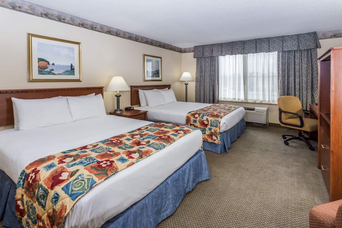 Habitación de hotel con dos camas, un escritorio, una silla y una ventana con cortinas.