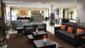 Un vestíbul d'hotel modern amb una taquilla d'accés, zona de seients i una cuina al fons.