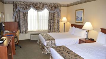 A hotel room with two beds, a desk, a chair, a lamp, and a painting on the wall.